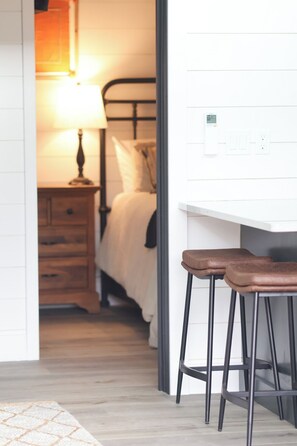 Una habitación con una cama, una mesita de noche con una lámpara y un taburete.
