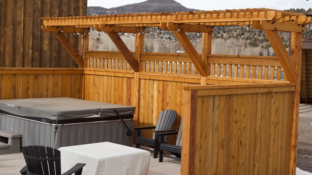 Une terrasse en bois avec un jacuzzi, un espace salon couvert et une vue sur les montagnes.