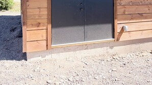 Une cabane en bois avec une grande porte sombre, une petite fenêtre et un sol recouvert de gravier.