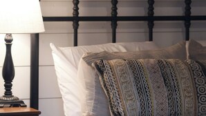 Un lit avec des coussins à motifs, une table de chevet en bois avec une lampe et un tableau encadré au mur.