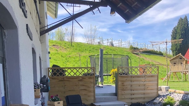 Un espacio al aire libre acogedor con muebles de madera y un barril, con vistas a una ladera verde.