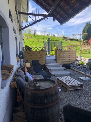 Un espace extérieur accueillant, aménagé avec du mobilier en bois et agrémenté d’un tonneau, offrant une vue sur une colline verdoyante.
