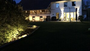 Una casa de dos pisos con techo inclinado, una chimenea visible y una entrada principal bien iluminada.