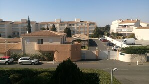 Zona residencial con edificios de apartamentos, un estacionamiento cerrado y una camioneta blanca estacionada en la calle.