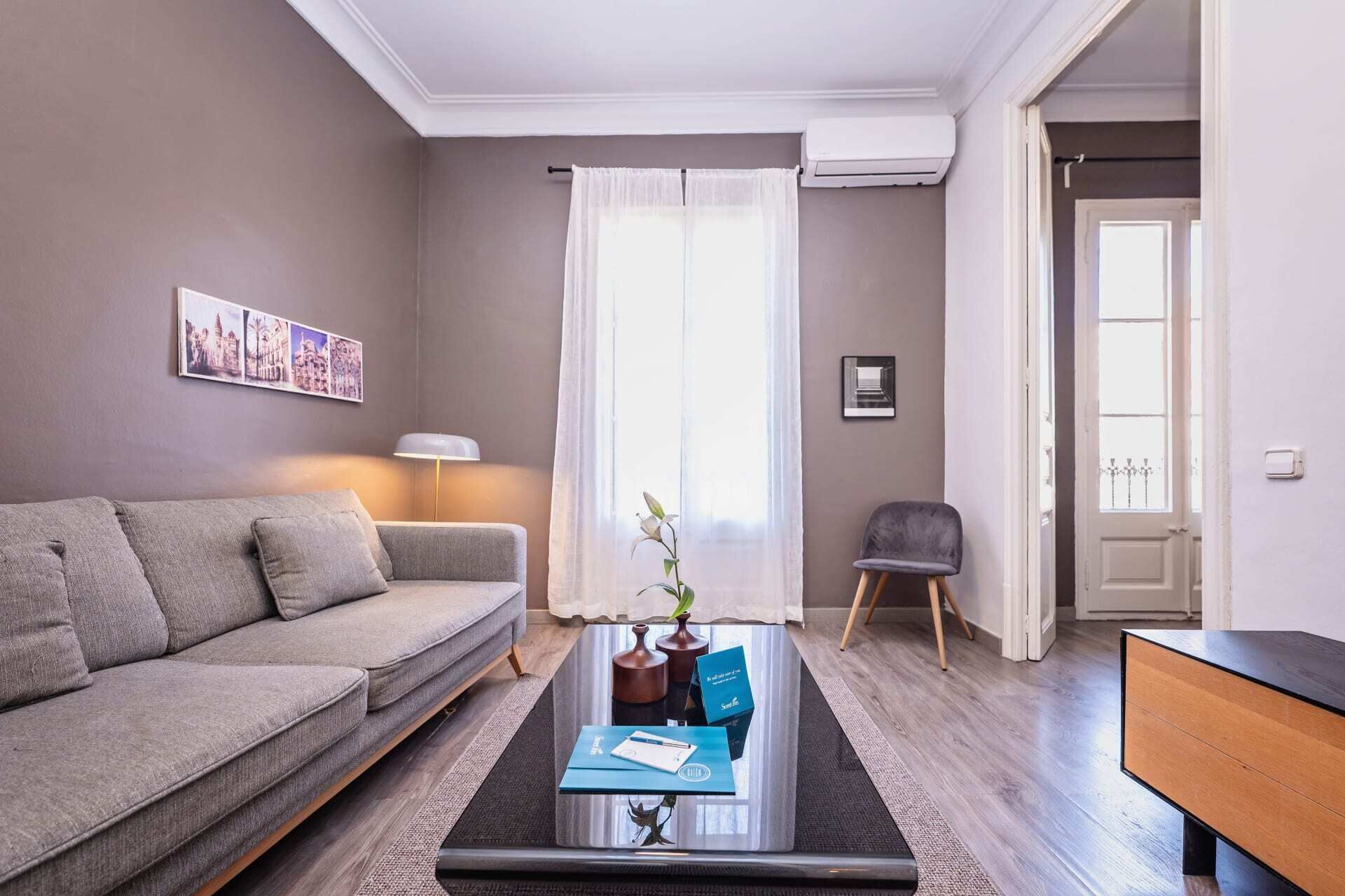 Ein modernes Wohnzimmer mit einem grauen Sofa, einem Couchtisch mit Dekoration, einer Lampe und einer Tür zu einem weiteren Raum.