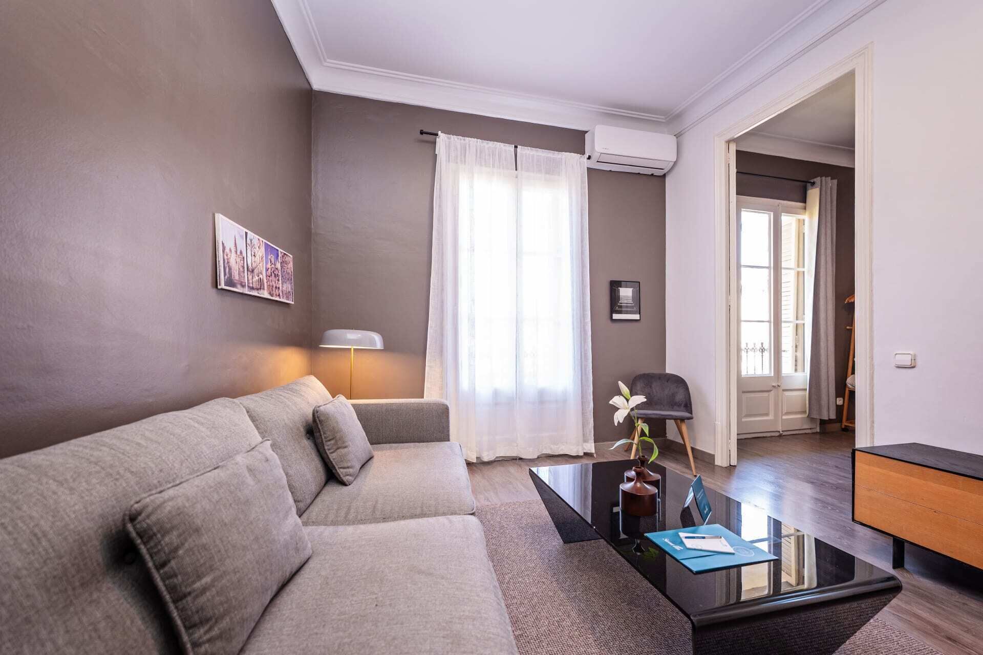 Un salon moderne avec un canapé gris, une table basse en verre et une lampe.