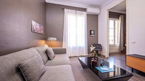 Ein modernes Wohnzimmer mit grauem Sofa, einem Glastisch und einer Lampe.