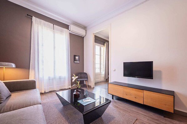 A modern living room with a sofa, a coffee table, a TV, and a wooden cabinet. - Sweett | Rocafort 403 (Barcelona)