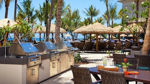 Un espace extérieur aménagé pour les repas, avec des parasols en chaume, des meubles en osier et un coin barbecue.