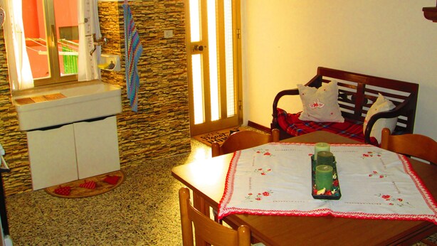 A cozy kitchen with a stone wall, a wooden dining table with a floral tablecloth, and a wooden chair. - Apartment "La casa dei nonni" (Acqualagna)