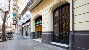 Une rue bordée d’un immeuble remarquable, doté d’un grand portail orné, d’une devanture de magasin avec une enseigne verte et d’un espace réservé au stationnement des vélos.