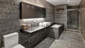 Ein modernes Badezimmer mit Marmorwand, einem großen Spiegel, einer weißen Toilette, einem Waschbecken und einer Duschkabine.