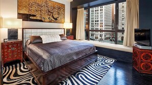 Ein modernes Schlafzimmer mit einem großen Bett, Blick auf die Stadt und einem dekorativen Gemälde.