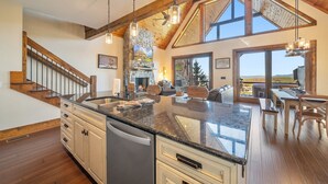 A spacious kitchen with a large island, wooden beams, and a stone fireplace. - Peregrine's Perch- amazing views, hot tub, outdoor fireplace, Eagles Nest amenities (Banner Elk)
