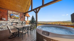 A wooden deck with a hot tub, stone fireplace, and a table with chairs. - Peregrine's Perch- amazing views, hot tub, outdoor fireplace, Eagles Nest amenities (Banner Elk)