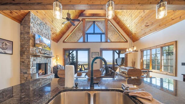 A spacious kitchen with a stone fireplace, a large window, and a high ceiling with wooden beams. - Peregrine's Perch- amazing views, hot tub, outdoor fireplace, Eagles Nest amenities (Banner Elk)