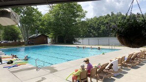 En swimmingpool med folk som simmar och solar. Det finns solstolar och en liten byggnad i bakgrunden.