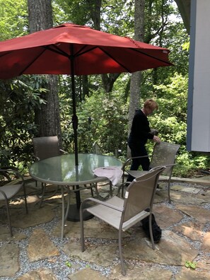 An outdoor patio with a glass table, metal chairs, and a red umbrella. - Mountain Cottage in Resort Setting (Newland)