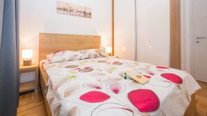 A neatly made bed with a patterned bedspread, a bedside lamp, and a framed picture on the wall. - Comfortable apartment located in the quier neighborhood in a new building . (Budva)