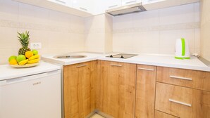 A kitchen with white cabinets, a wooden countertop, a sink, and a fruit bowl containing a pineapple and bananas. - Comfortable apartment located in the quier neighborhood in a new building . (Budva)