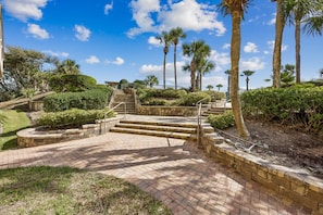 A landscaped area with a brick pathway leading up to a set of stairs, surrounded by palm trees and greenery.