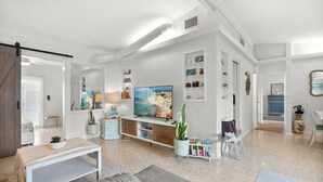 Uma sala de estar moderna com uma televisão de tela grande, um sofá branco, uma mesa de centro e uma estante de livros.