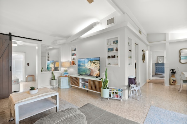 Een moderne woonkamer met een grote flatscreen-televisie, een witte bank, een salontafel en een boekenkast.