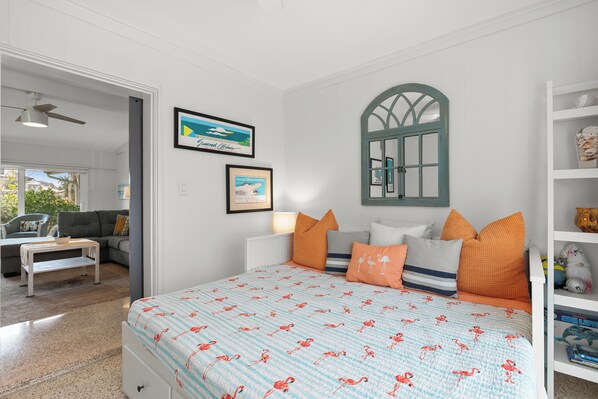 Un dormitorio con cama, ventana, estantería y puerta que da a otra habitación.