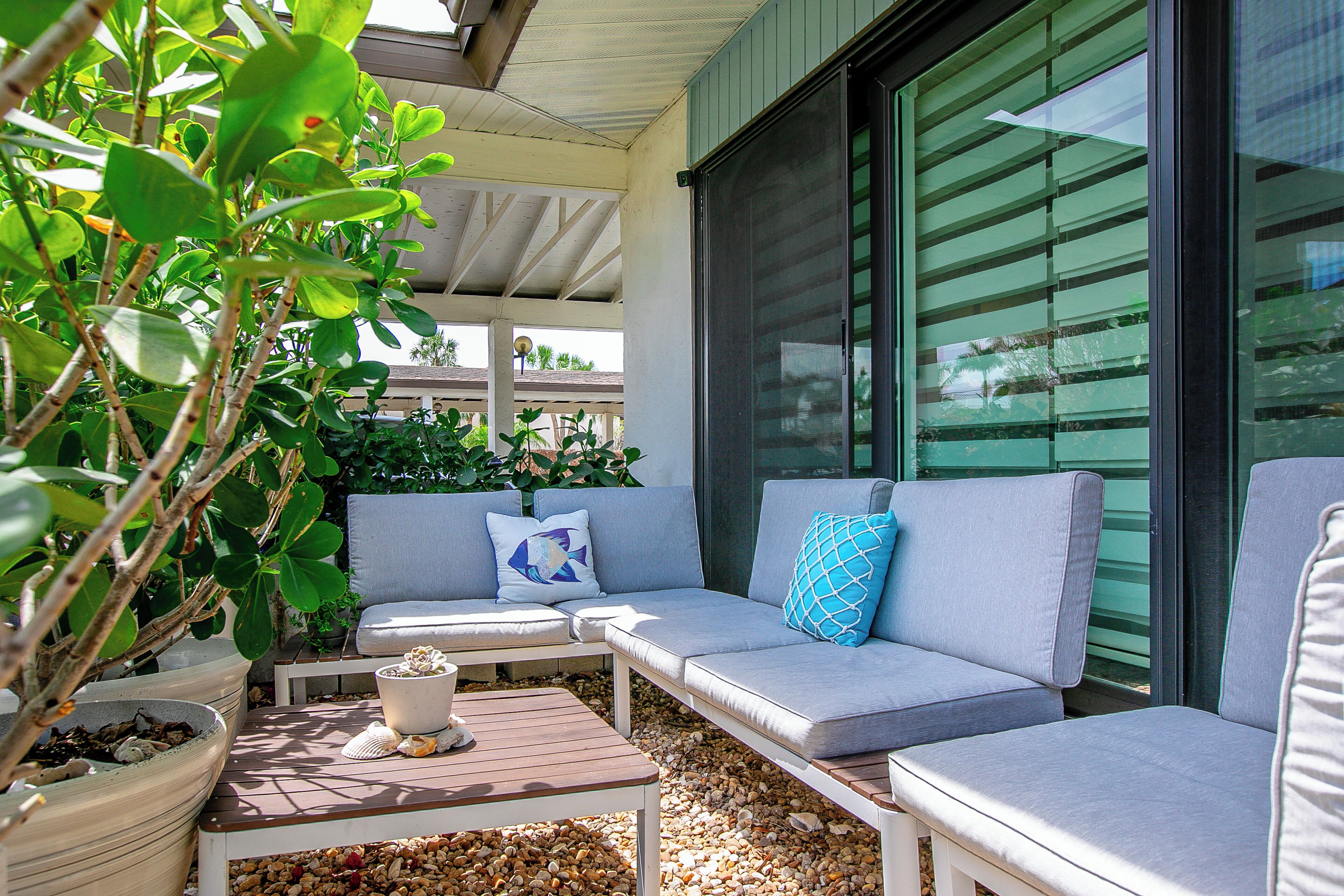 An outdoor seating area with a cushioned sofa, a wooden table, and a potted plant.
