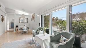Uma sala de estar ampla com uma mesa de jantar, duas poltronas cinzas, uma toalha de mesa branca e um vaso de flores.