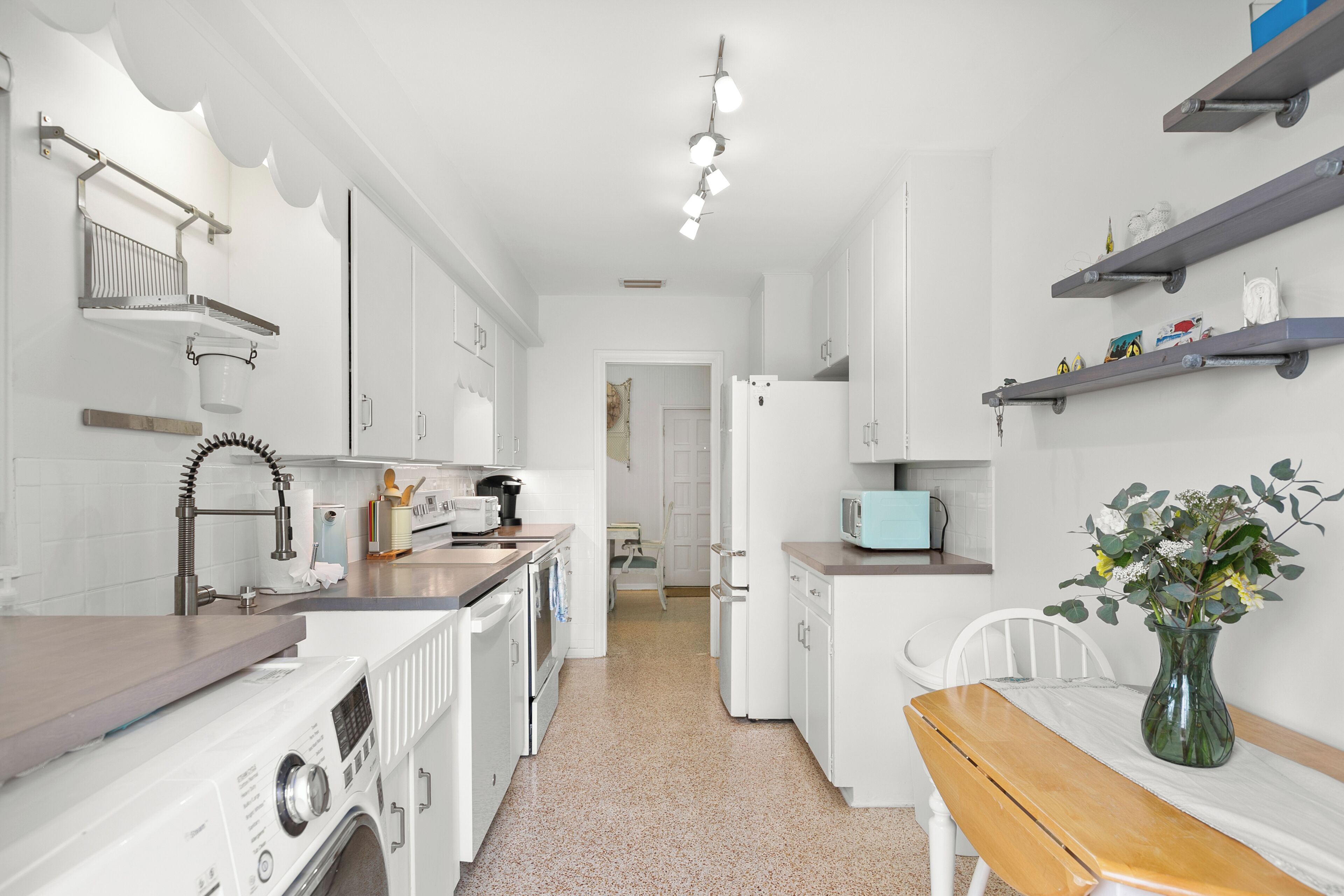 A modern kitchen with white appliances, a wooden bench, and a vase with flowers.