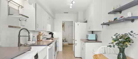 A modern kitchen with white appliances, a wooden bench, and a vase with flowers.