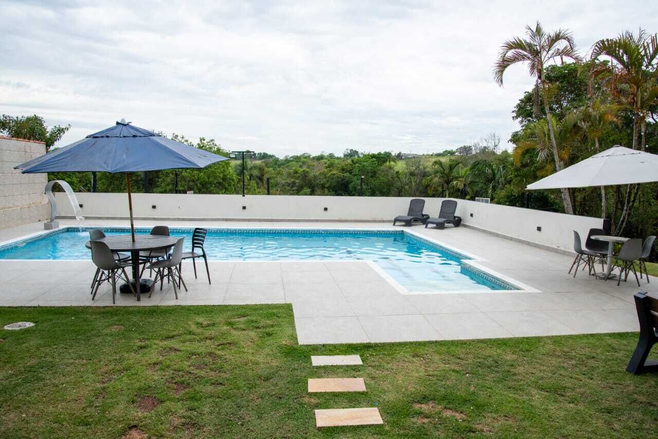 Una piscina rectangular amb una terrassa enrajolada, envoltada per una paret blanca. Hi ha dos ombrelles que fan ombra, una taula amb cadires, i una zona enjardinada amb pedres que condueixen a la piscina.