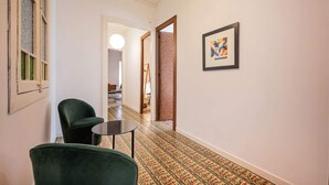 Ein Flur mit gemustertem Bodenbelag, einem gerahmten Kunstwerk an der Wand und zwei grünen Stühlen.