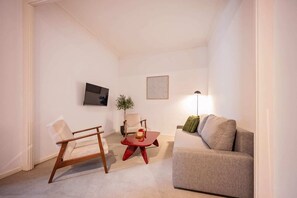 Een woonkamer met een bank, een fauteuil, een tafeltje, een vloerlamp en een plant.