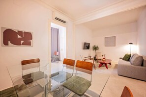 A modern living room with a glass dining table, a grey sofa, and a red coffee table. - Sweett | Rocafort 304 (Barcelona)