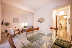 A modern living room with a glass dining table, a sofa, and a TV. - Sweett | Rocafort 304 (Barcelona)
