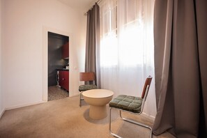 A hotel room with a round table, a green cushioned chair, a red cabinet, and a window with curtains. - Sweett | Rocafort 304 (Barcelona)
