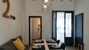 Ein moderner Wohnbereich mit Essplatz, einer gelben Kissen auf einer Couch, der großen Zahl '2' an der Wand und einer geometrischen Leuchte.
