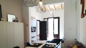 Ein moderner Essbereich mit einem weißen Tisch für vier Personen, schwarzen Tischsets und einem schwarzen Stuhl. Es gibt eine Couch mit einer gelben Tagesdecke und einen kleinen Tisch mit einer Lampe.