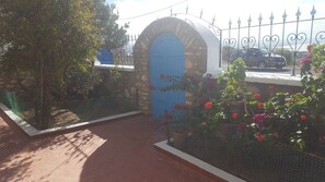 A stone building with a blue door, surrounded by a metal fence and flowering plants.