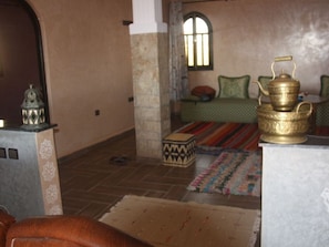 A room with a patterned rug, a sofa, a small table with a decorative item, and a window with a view.