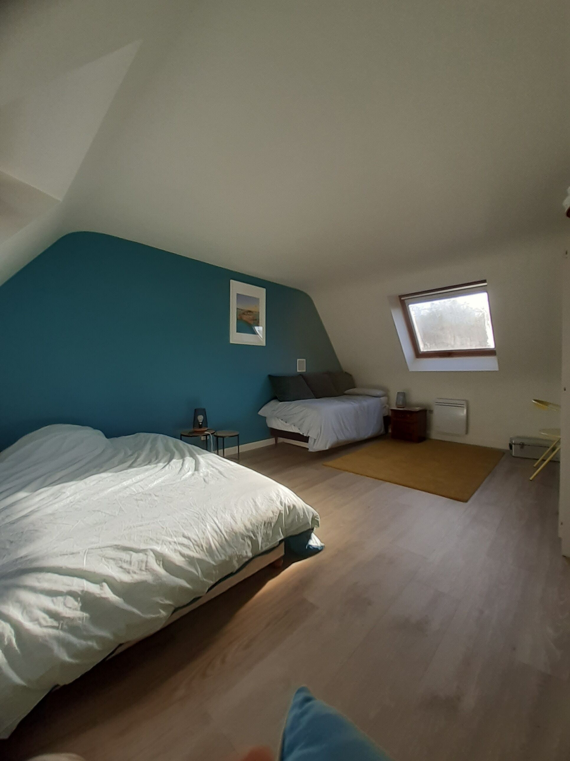 Un dormitorio con una cama grande, una cama más pequeña, un tragaluz y un cuadro en la pared.