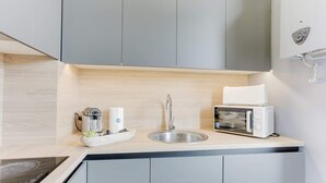 Et kompakt køkken med vask, kaffemaskine, mikroovn og brødrister.