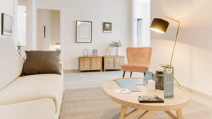 En moderne stue med en sofa, et rundt sofabord og en lænestol. To træsideborde med dekorative genstande, og billeder hænger på væggen.