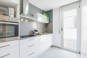 A modern kitchen with a built-in oven, microwave, and stove, a sink, and a sliding door leading to a balcony.