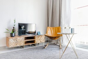 Ein modernes Wohnzimmer mit Fernseher, einer Couch, einem kleinen Tisch mit Gläsern und einer Topfpflanze.