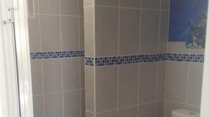 A bathroom with a shower, toilet, and a blue rug. - Studio any comfort. (Terre de haut les saintes)