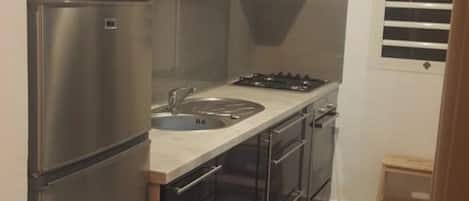 Cocina pequeña con refrigerador, estufa, lavaplatos y armarios.