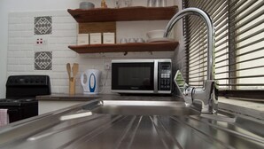 A kitchen with a stainless steel sink, a microwave, a stove, and wooden shelves above the counter.